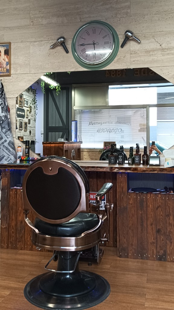 Puesto de barbero con sillón vintage, espejo octogonal, reloj de pared y pared de piedra en Hidalgo Junior.